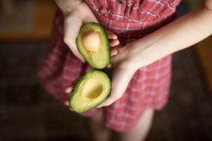 person holding two sliced avocados